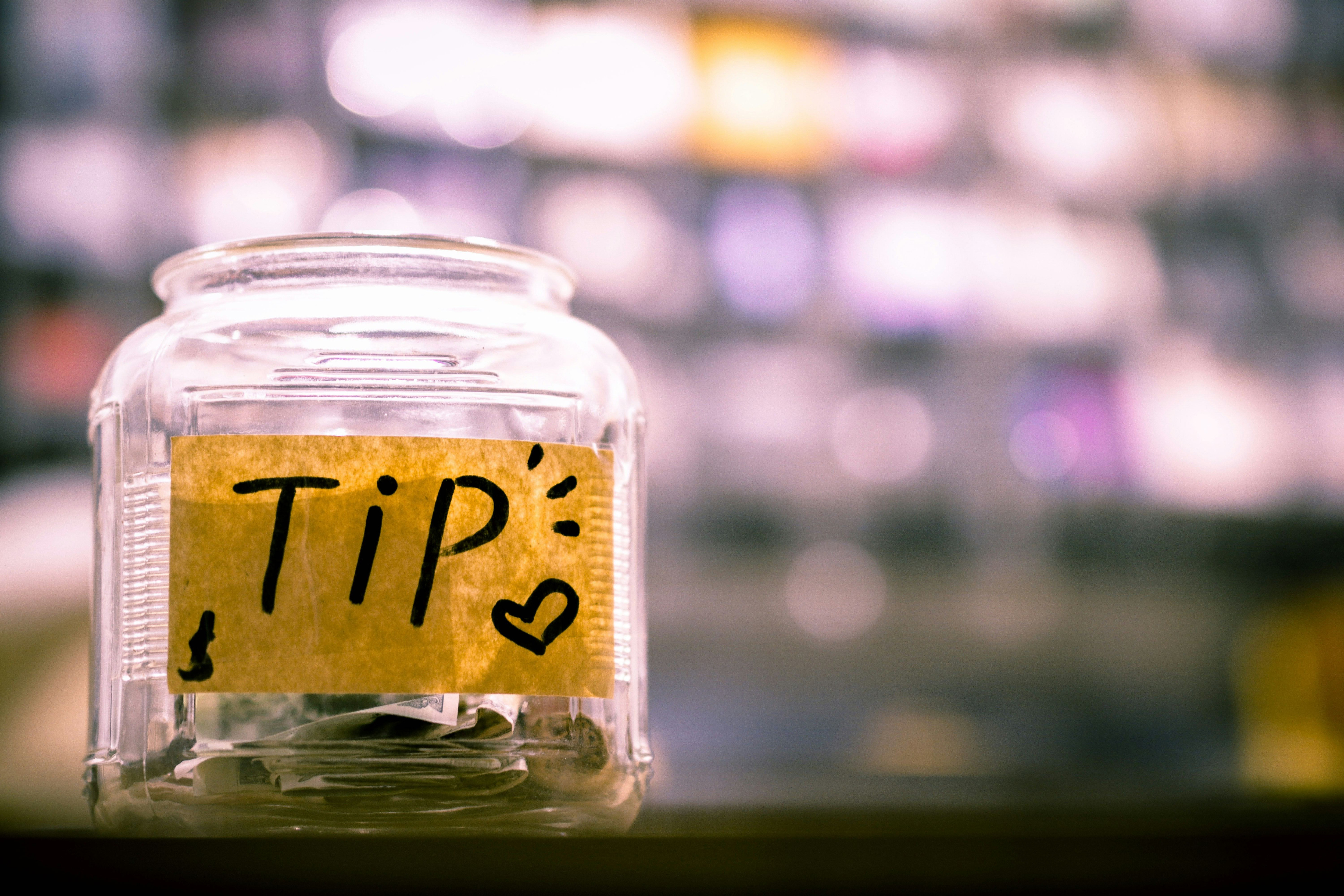  Glass jar labeled “Tips” filled with cash, symbolizing tipping house cleaners